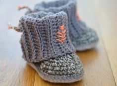 a pair of gray crocheted baby booties sitting on top of a wooden floor