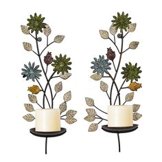 two candles are sitting next to each other with leaves and flowers on the candle holders