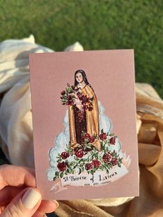 a person holding up a card with an image of the virgin mary on it and roses