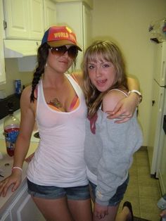 two young women standing next to each other in a kitchen, one with her arm around the other's shoulder