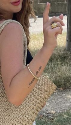 a woman with a small tattoo on her arm holding a straw bag and pointing to the side