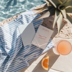 an orange slice next to a book on a towel near a pool with a drink