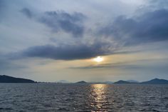 the sun is setting over the ocean with mountains in the distance and water below it