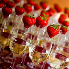 many glasses filled with wine and strawberries on top of eachother are lined up