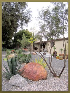 a rock and some plants in front of a house