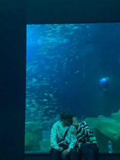 a man sitting on a bench in front of a large aquarium filled with lots of fish