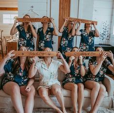 four women sitting on a couch holding up wooden planks in front of their faces