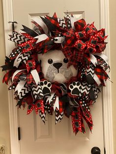 a teddy bear wreath with black and red bows on it's head is hanging on the front door