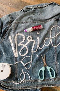 a denim jacket with the word bride written on it next to some scissors and thread