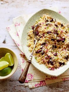 a bowl filled with rice, beans and limes next to a spoon on a napkin