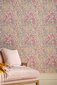 a pink chair sitting in front of a floral wallpaper