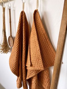 two brown towels hanging from hooks on a white wall next to wooden spoons and other kitchen utensils