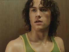 a young man with curly hair wearing a green tank top and looking at the camera