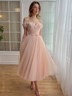 Embrace ethereal elegance with this pale peach tulle midi creation, a testament to delicate sophistication. The off-shoulder silhouette is adorned with intricately embroidered flowers, each petal embellished with tiny pearls, evoking enchanting beauty. Featuring a draped wrap bodice with structured corset and boning, it cinches at the waist, enhanced by a decorative bow belt. Practical yet chic, it includes inseam pockets and is designed in a midi-length style, with layers of tulle underneath for added volume. The lace-up back ensures a flawless fit, making this piece an exquisite choice for special occasions, where its wearer is destined to shine. Ethereal Pink Evening Dress, Elegant Pink Tulle Corset Dress, Elegant Pink Tulle Fairy Dress, Peach Semi-stitched Wedding Dress, Teuta Matoshi Pink Dress, Peach Prom Dresses, Juliet Rose, Petal Dress, Structured Corset