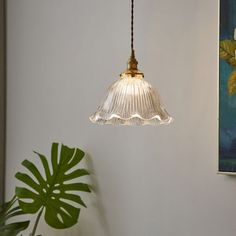 a lamp hanging from a ceiling next to a potted plant and painting on the wall