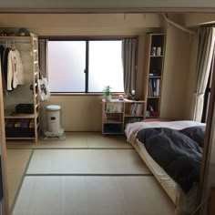 a room with a bed, desk and shelves in it next to a large window