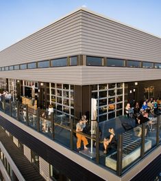 people sitting and standing on the balcony of a building with glass doors, eating outside