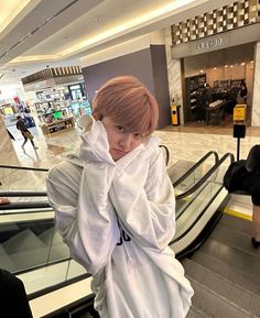 a boy in a white outfit is standing on an escalator with his hands over his face