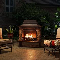 an outdoor fireplace lit up at night with two chairs and a table in the foreground