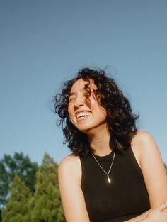 a woman with curly hair is smiling and holding her arms crossed in front of the camera