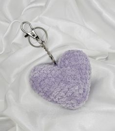 a purple heart shaped keychain laying on a white satin