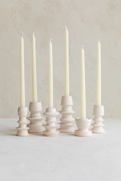 six white candles are lined up in a row on a plain surface, with one candle lit and the other turned upside down