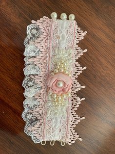 a piece of lace with pink flowers and pearls on the edge is laying on a wooden surface