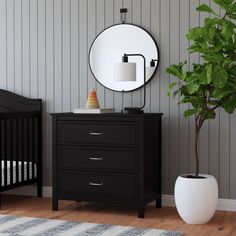 a black dresser with a mirror and a potted plant in it next to a white crib