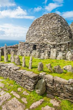 an old stone building with grass and rocks around it