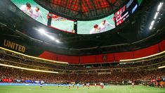 a large stadium filled with lots of people watching soccer on big screen tv's