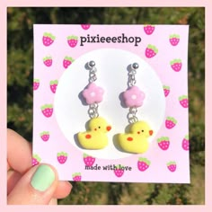 a pair of yellow rubber ducky earrings with pink polka dots on them, sitting in front of a card