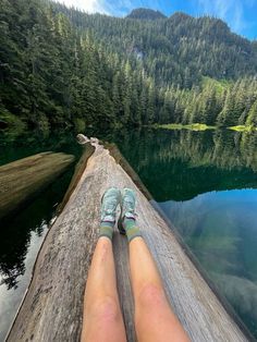 someone's feet resting on the edge of a log near a lake