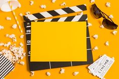 popcorn, sunglasses and movie claps on a yellow background with white striped paper next to them