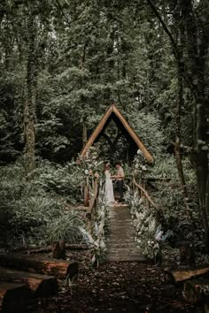 a bride and groom standing on a wooden bridge in the woods surrounded by greenery