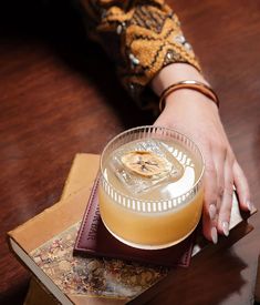 a woman's hand on top of a drink in a glass next to a stack of books