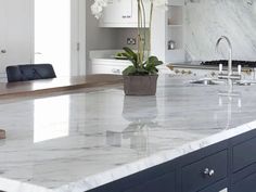 a large kitchen with marble counter tops and white cabinets in the background, along with a potted plant on an island