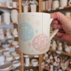 a person holding a coffee mug in front of a shelf full of pottery and other items