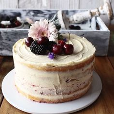 a white cake with berries and flowers on top sits on a plate in front of a wooden box