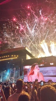 a woman standing on top of a stage next to a large screen with fireworks in the sky