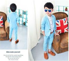 a little boy in a blue suit and sunglasses standing next to a brown leather chair