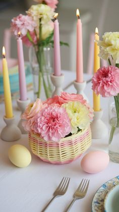 pink and yellow flowers in a basket on a table with candles, plates and utensils