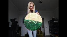 a woman holding up a painting with trees on it