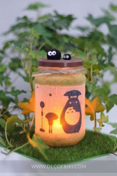 a mason jar with two eyes and a penguin on it sitting in the grass next to some plants