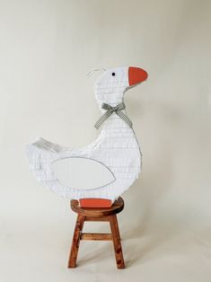 a paper cut out of a duck sitting on a stool with an orange seat cushion