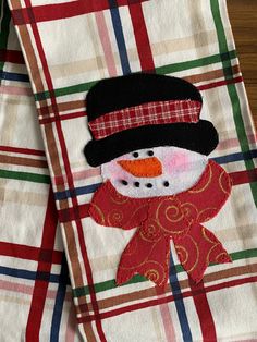 the snowman is wearing a black hat and red scarf with green, white, and blue plaid