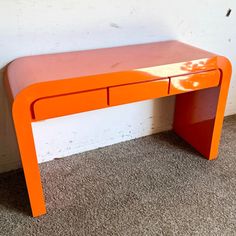 an orange desk sitting on top of a carpeted floor next to a white wall