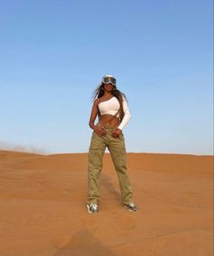 a woman standing in the middle of a desert with her hands on her hips and wearing goggles