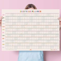 a woman holding up a calendar for the new year in front of her face, against a pink background