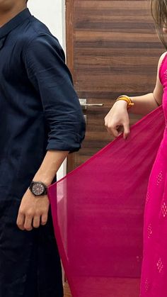 a man and woman standing next to each other in front of a door holding a pink dress