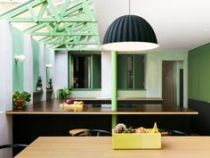 a kitchen with green walls and wooden table in front of the counter top, along with a black pendant light hanging from the ceiling